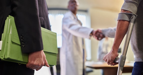 Man with crutch shaking hands with a physician while standing beside man with legal documents