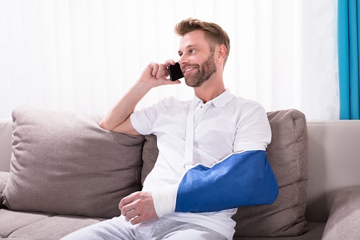 Young man with arm in sling, seated on couch talking on cell phone